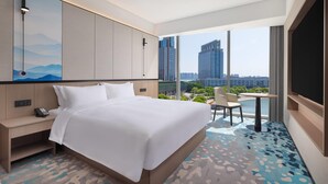 A hotel room with a large bed, a desk with a phone, a small table with two chairs, and a large window offering a city view. - Days Hotel By Wyndham Suzhou Dushu Lake (Suzhou)