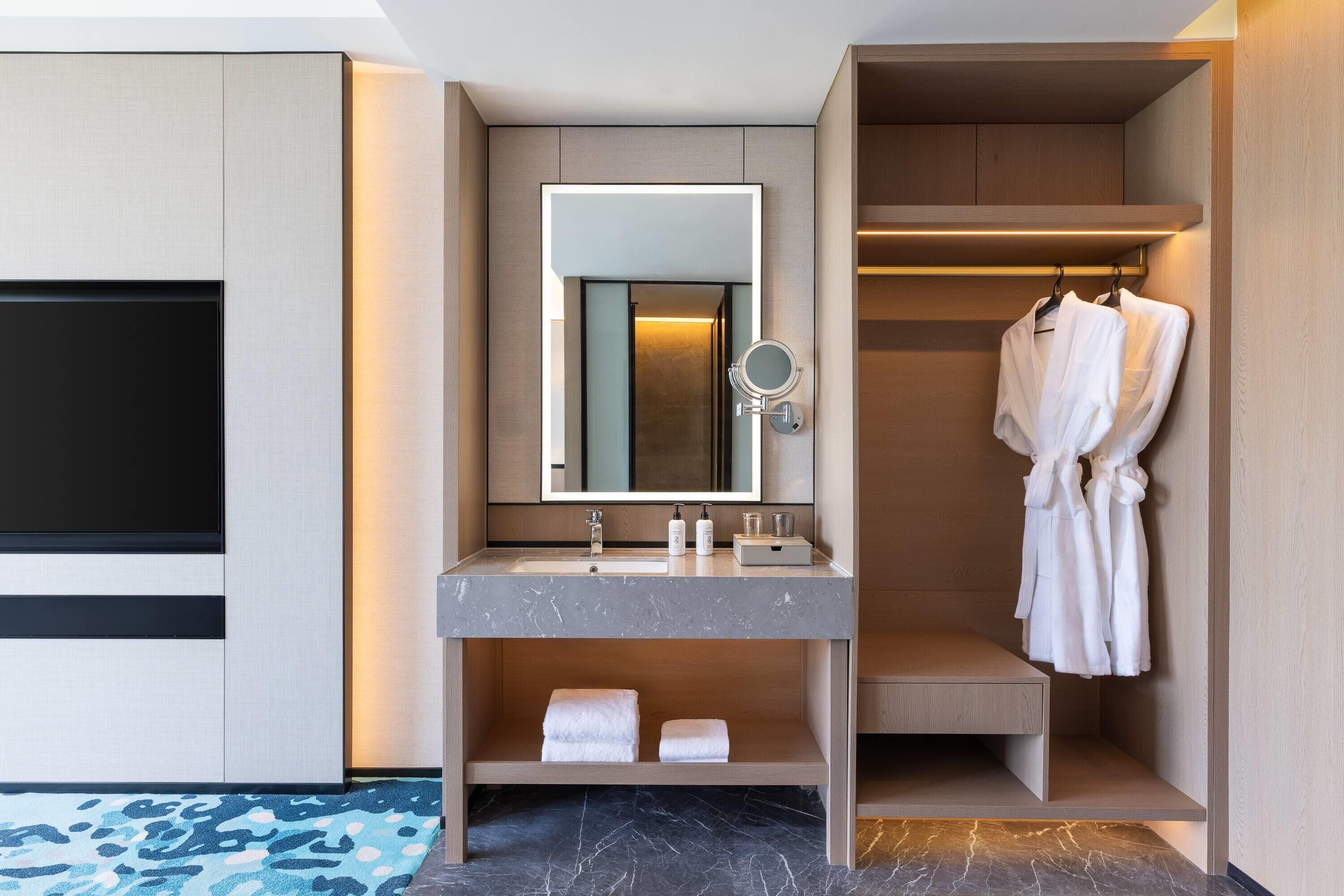 A modern bathroom with a marble sink, a large mirror, and a robe hanging on a rack.