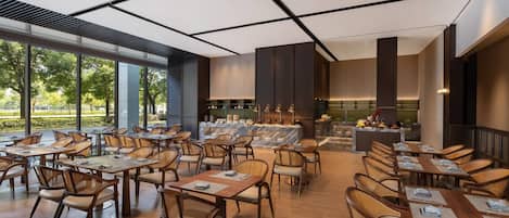 A modern restaurant with a long dining area, wooden tables, and chairs, and a bar area with a marble countertop.