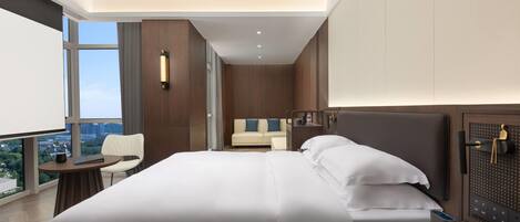 Une chambre d’hôtel moderne dotée d’un grand lit, d’un bureau avec une chaise, d’une petite table et offrant une vue sur la ville grâce à de grandes fenêtres.