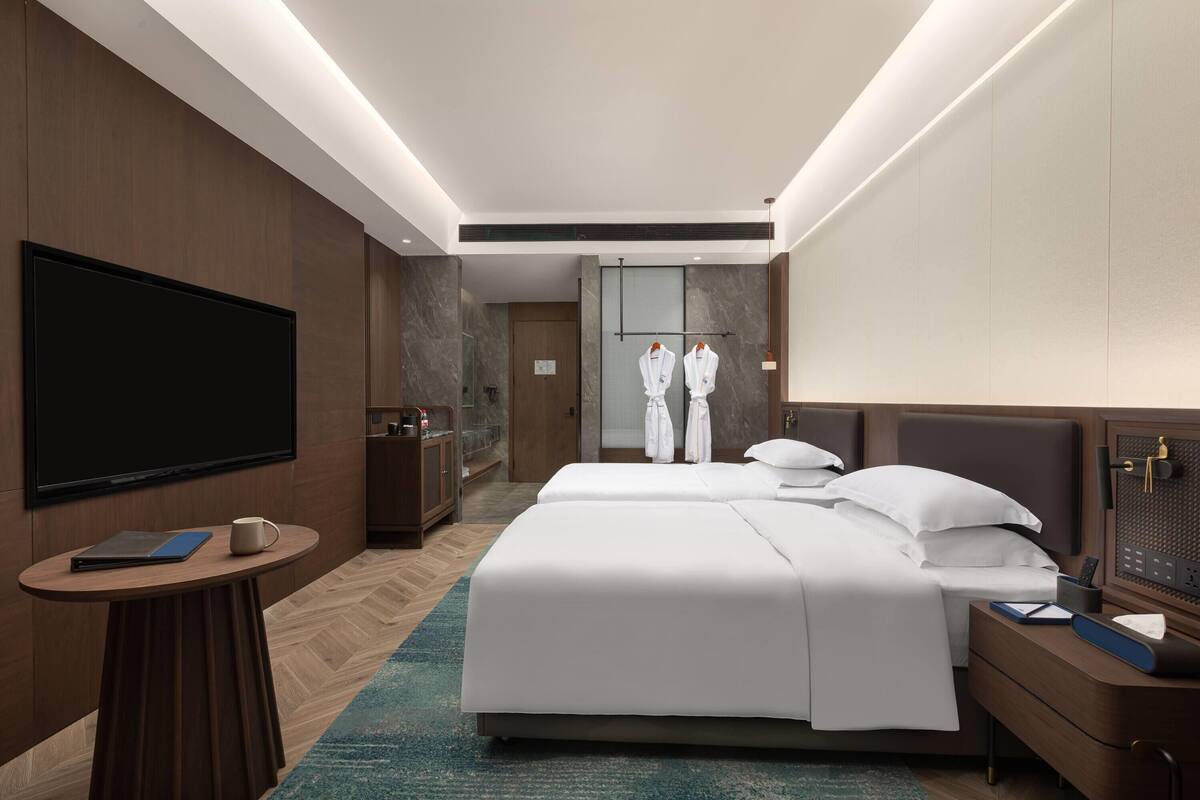 A modern hotel room with a large bed, bedside tables, a flat-screen TV, and a bathroom visible through an open door.