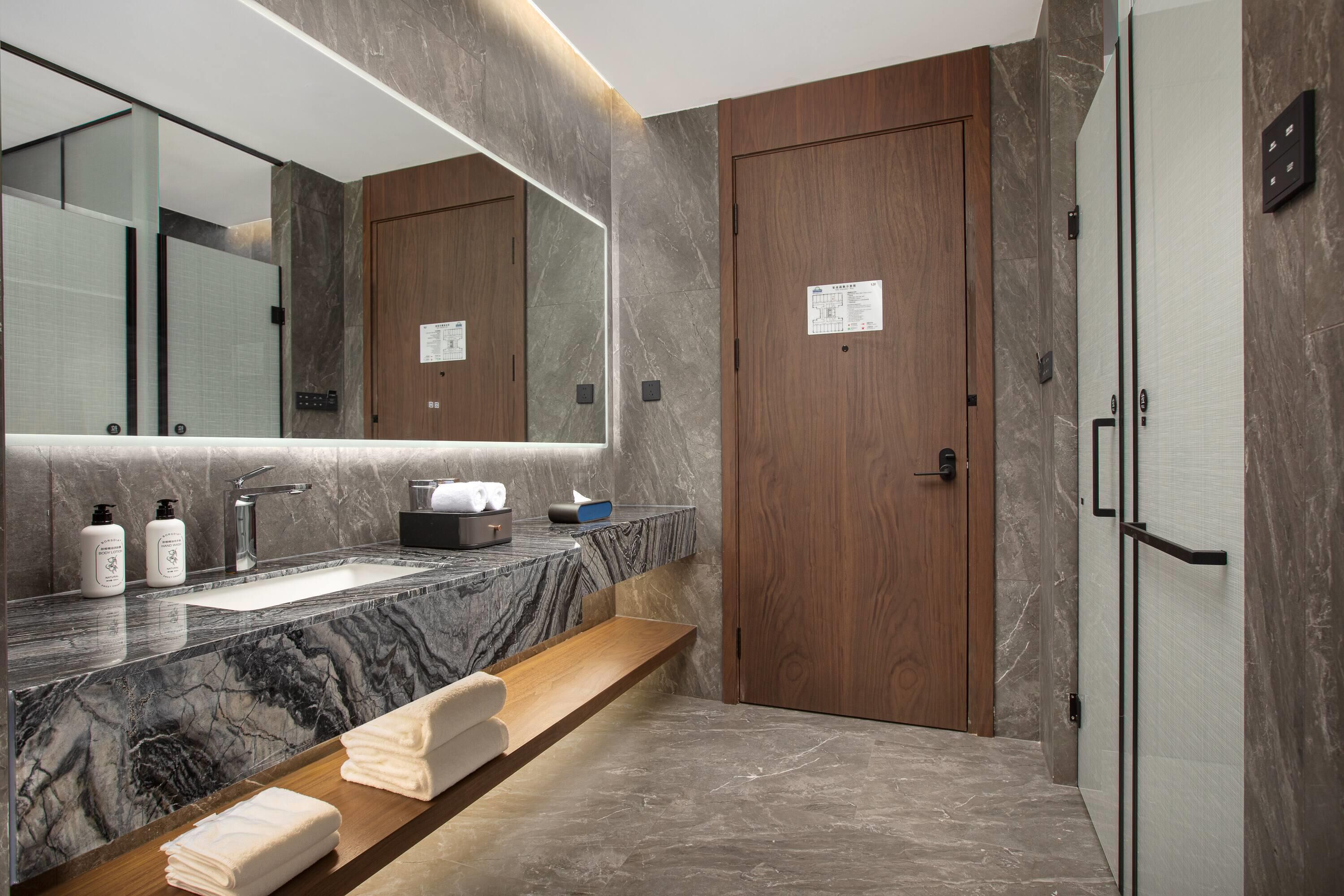 A modern bathroom with a marble sink, wooden vanity, and a large mirror.