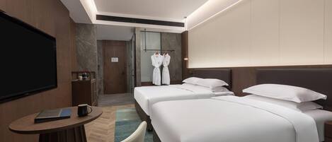 A hotel room with two beds, a TV, a desk with a laptop and mug, and a robe rack.