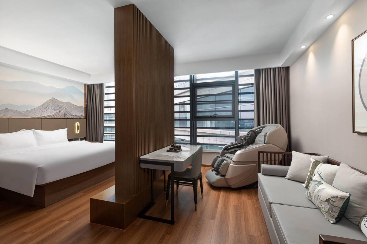 A modern hotel room with a bed, a desk, a sofa, and a massage chair.