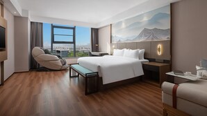 Ein modernes Hotelzimmer mit einem großen Bett, einem Massagesessel, einem Schreibtisch und einem großen Fenster mit Blick auf die Stadt.