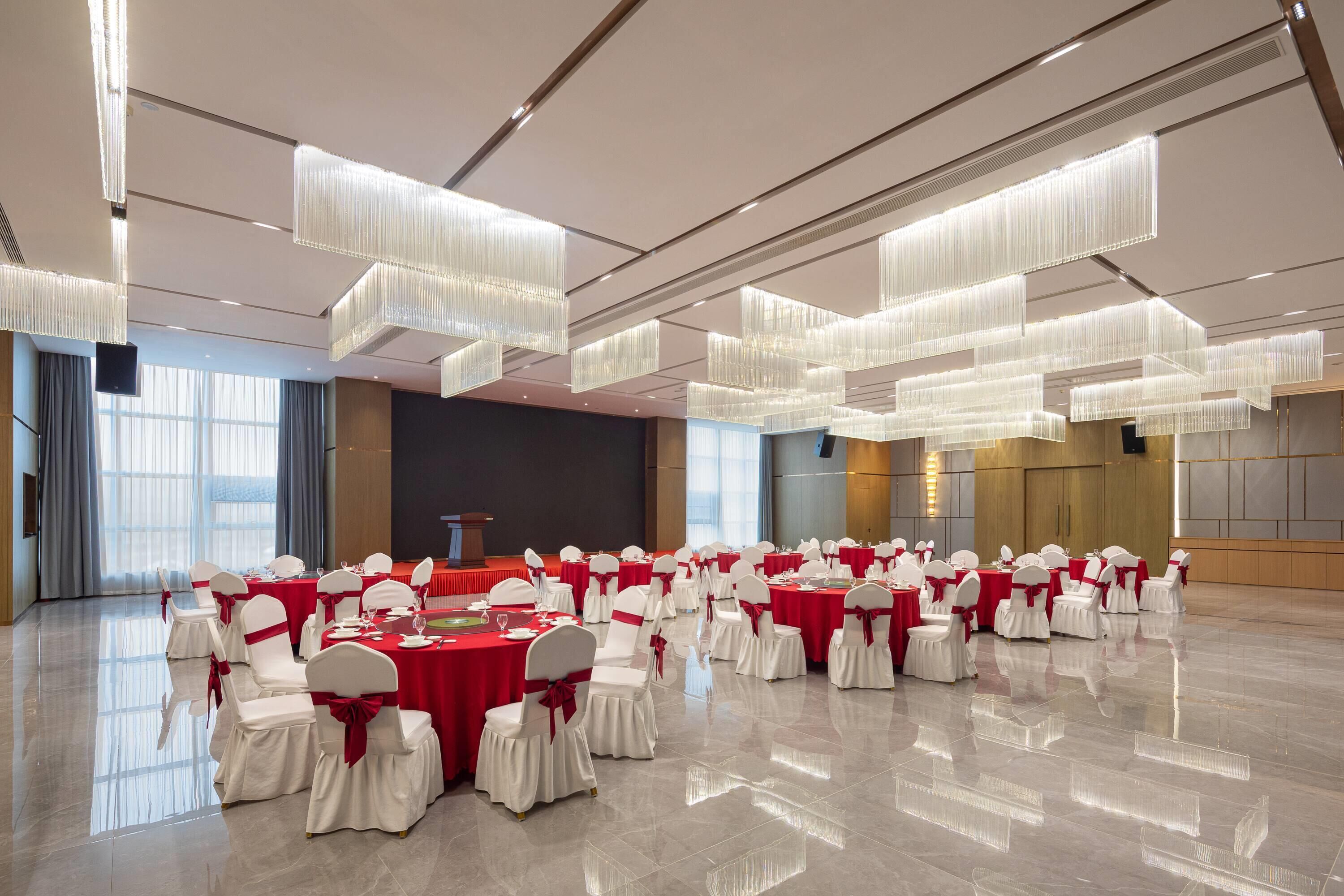 A spacious banquet hall with rows of tables and chairs, a podium, and modern lighting fixtures.