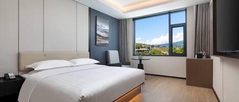 A modern hotel room with a large bed, a desk, and a view of the mountains.