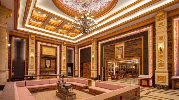 Un lobby lujoso con una zona de estar central, techo ornamentado y un gran candelabro.