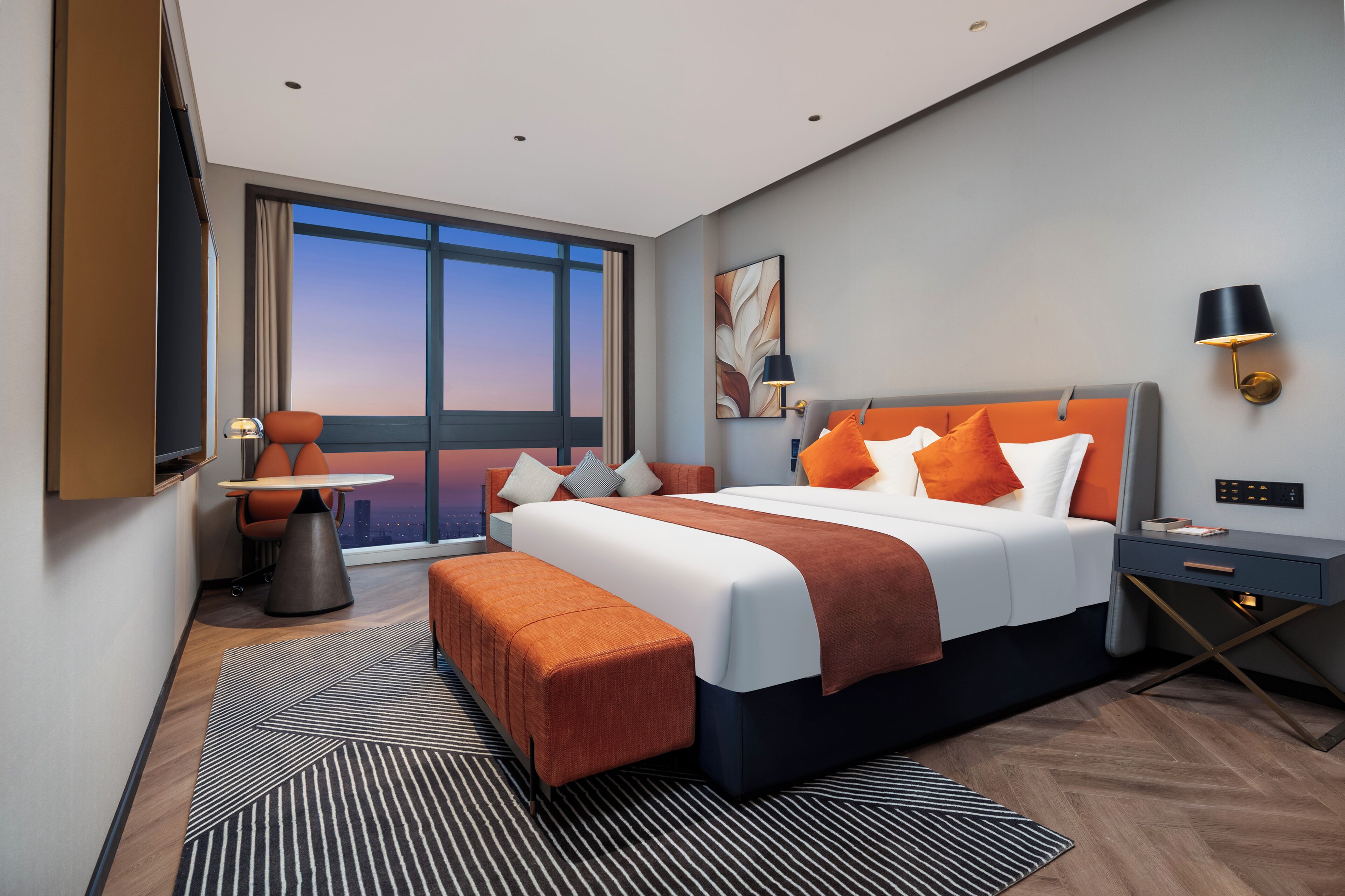 A modern hotel room with a large bed, a desk, a chair, and a view of the cityscape.
