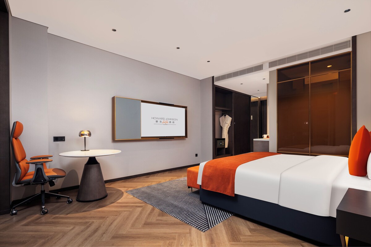 A modern hotel room with a bed, a desk, a chair, a round table, and a wardrobe.