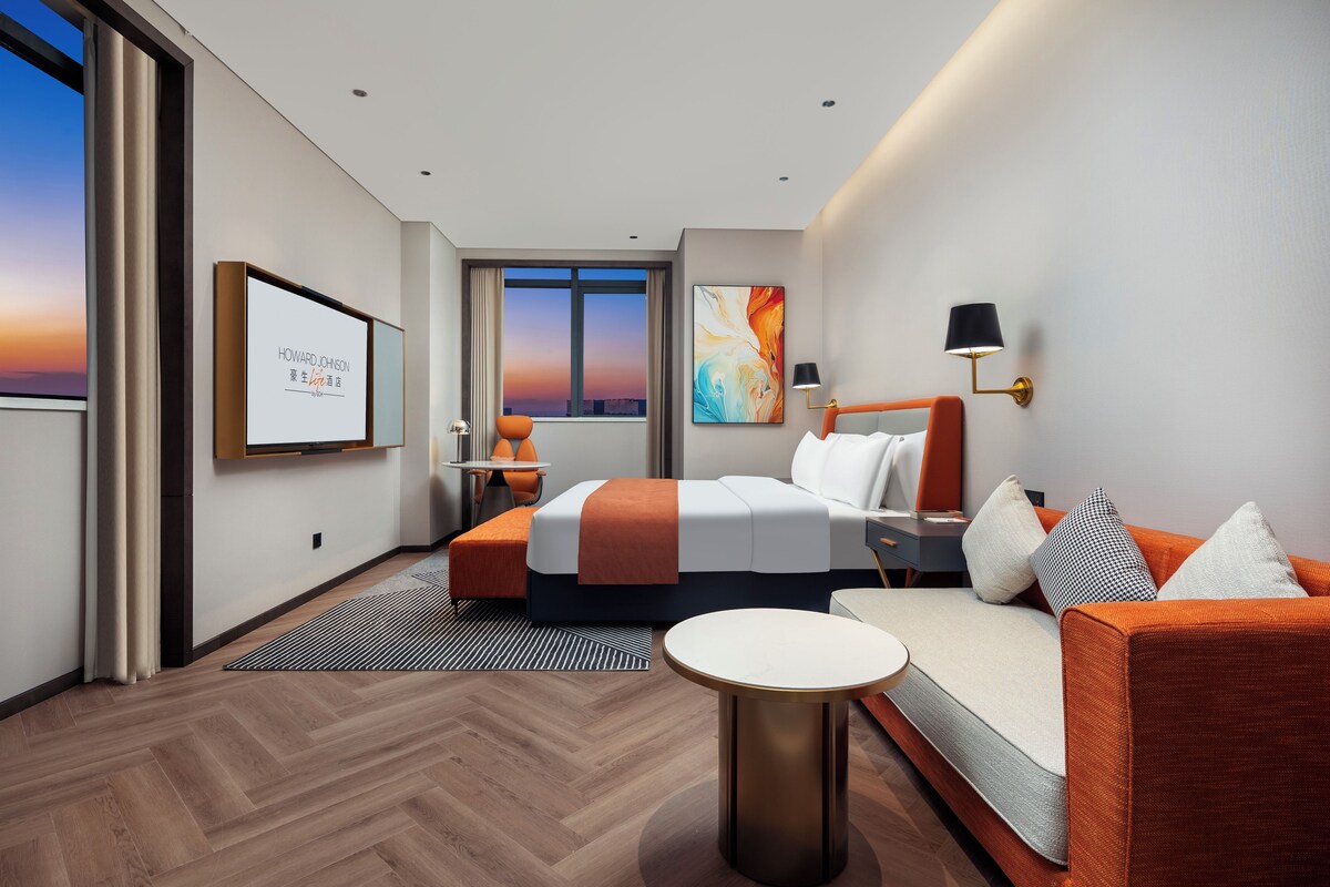 Habitación de hotel moderna con cama, sofá, una mesita y una pantalla de televisión mostrando un mensaje.