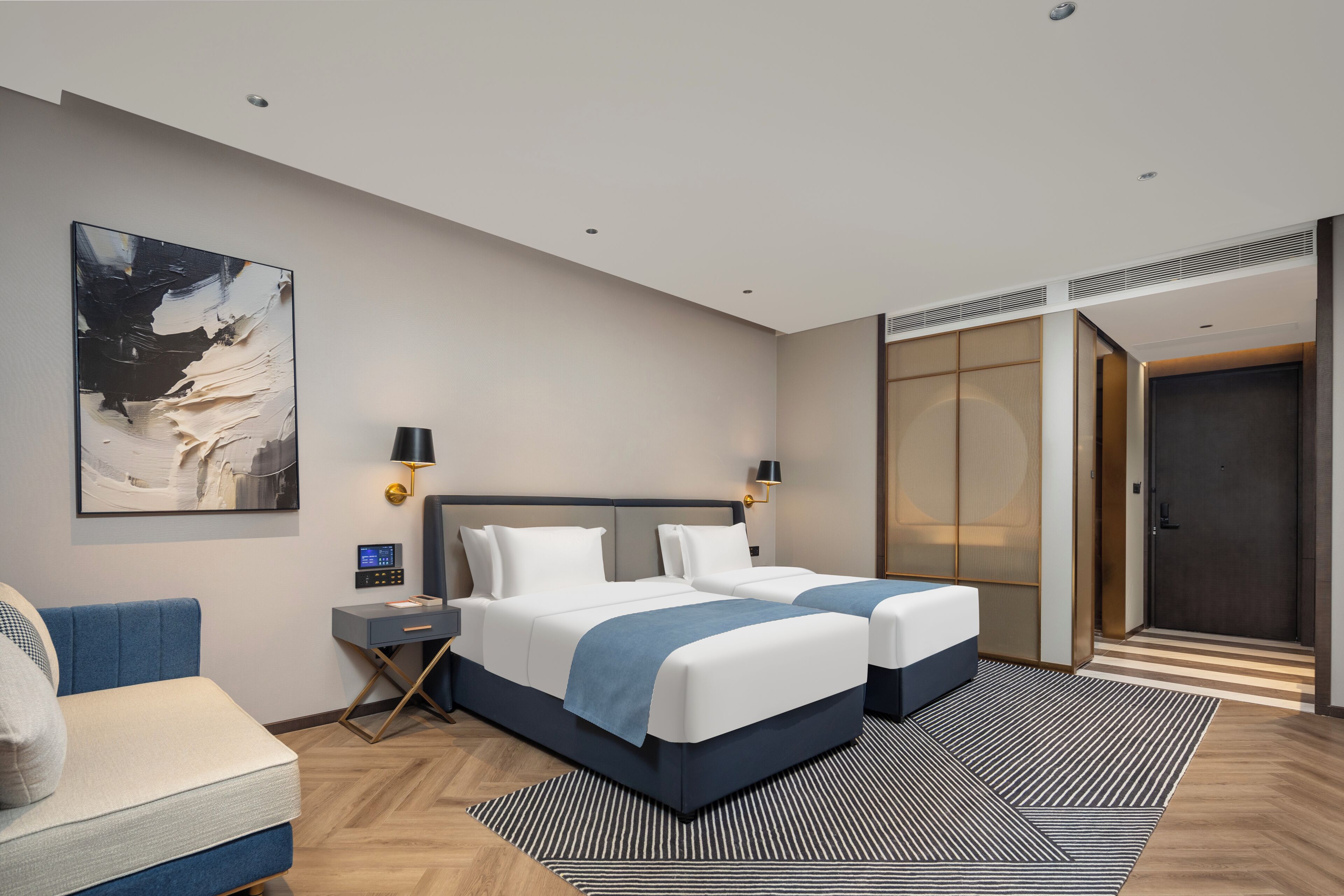 Ein Hotelzimmer mit zwei Betten, einem Schreibtisch, einem Stuhl, einem großen abstrakten Gemälde und einer Schiebetür zu einem Schrank.