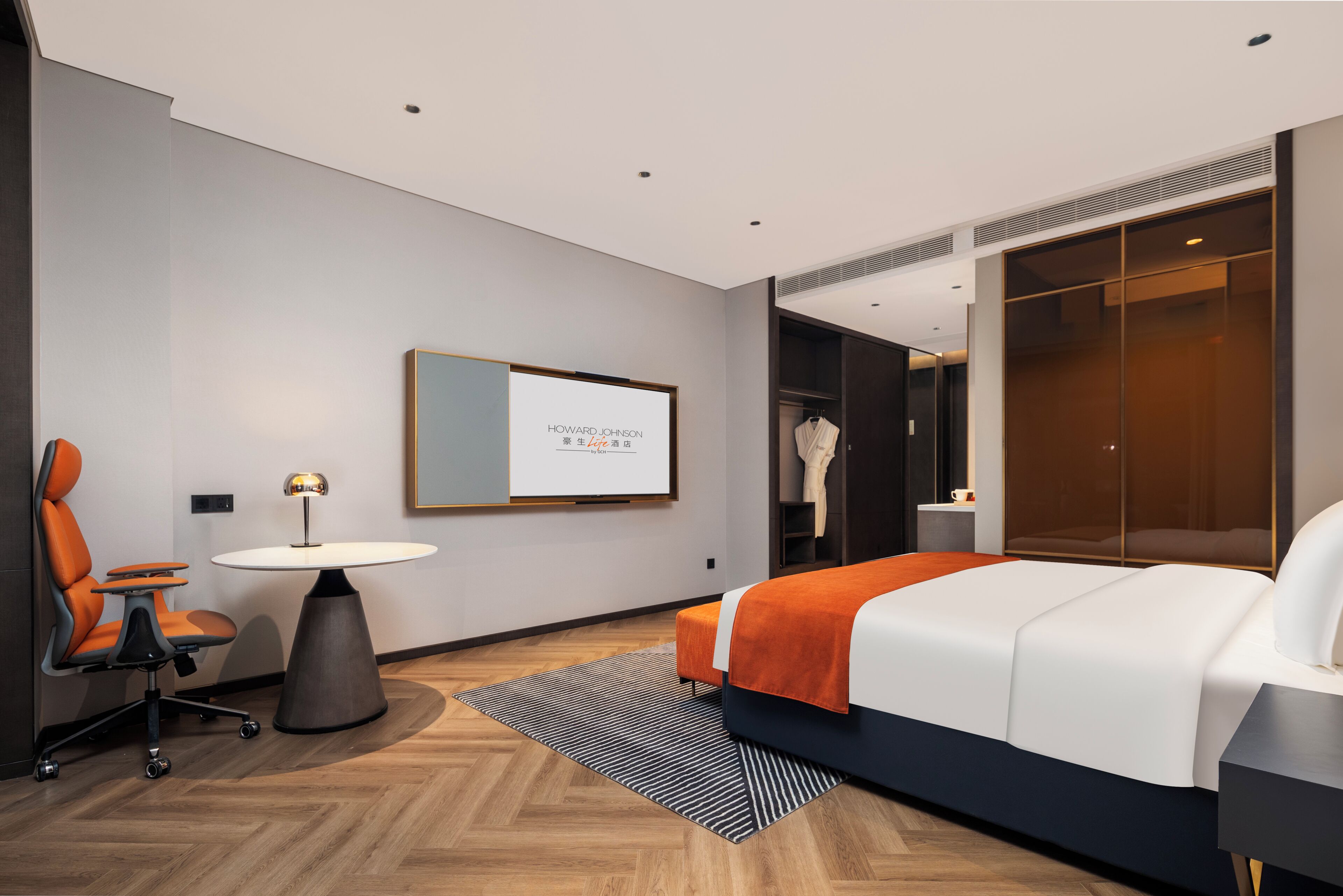 A modern hotel room with a bed, a desk, a chair, and a wardrobe.