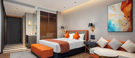 A modern hotel room with a large bed, a sofa, a coffee table, and a painting on the wall.