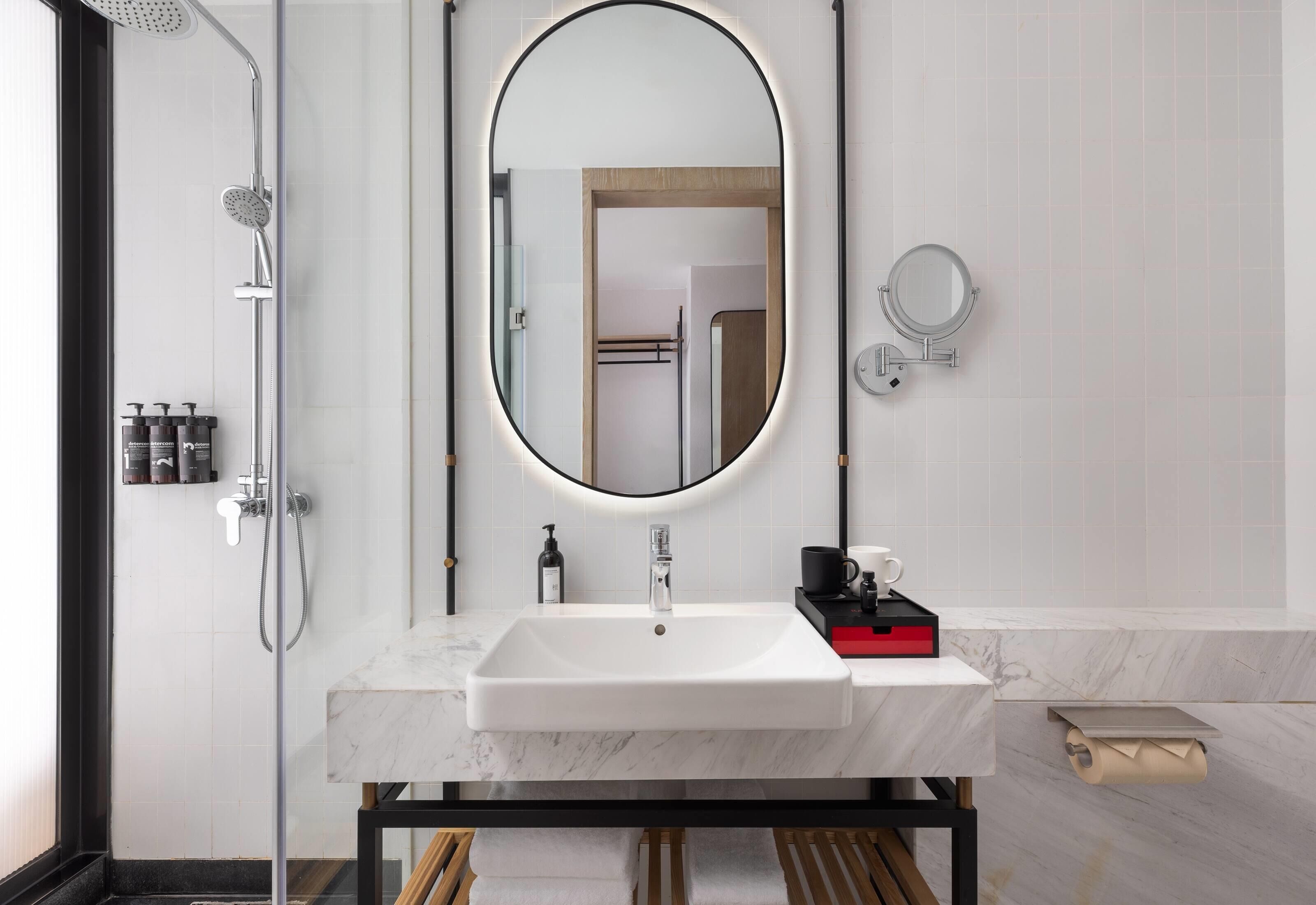 Een moderne badkamer met een wit wastafel, een grote spiegel, een handdouche en een kleine ronde spiegel aan de muur.