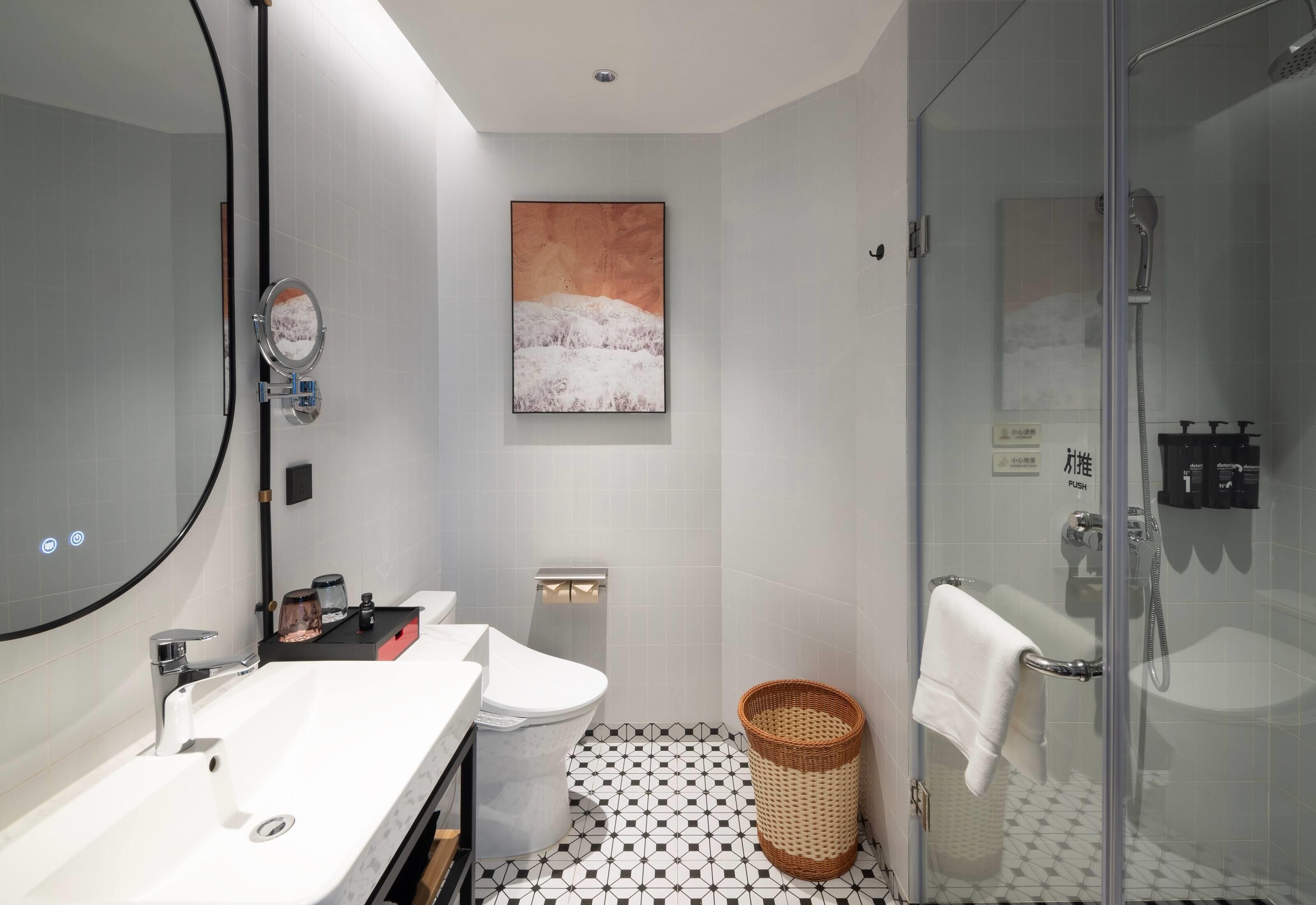 A modern bathroom with a white sink, a toilet, a glass shower enclosure, and a wall-mounted mirror.
