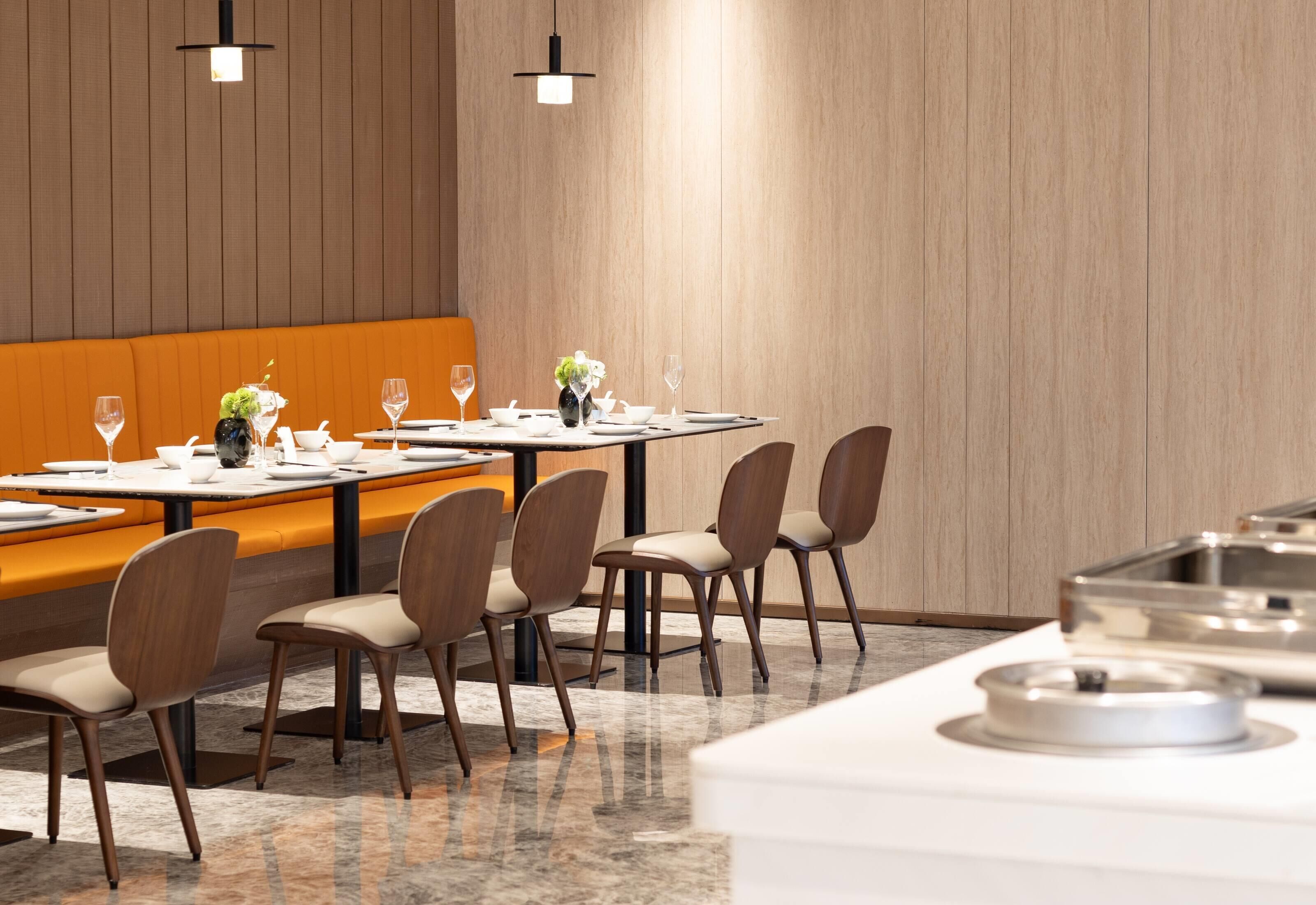 Un comedor moderno con paneles de madera, un banco central naranja y suelo de mármol.
