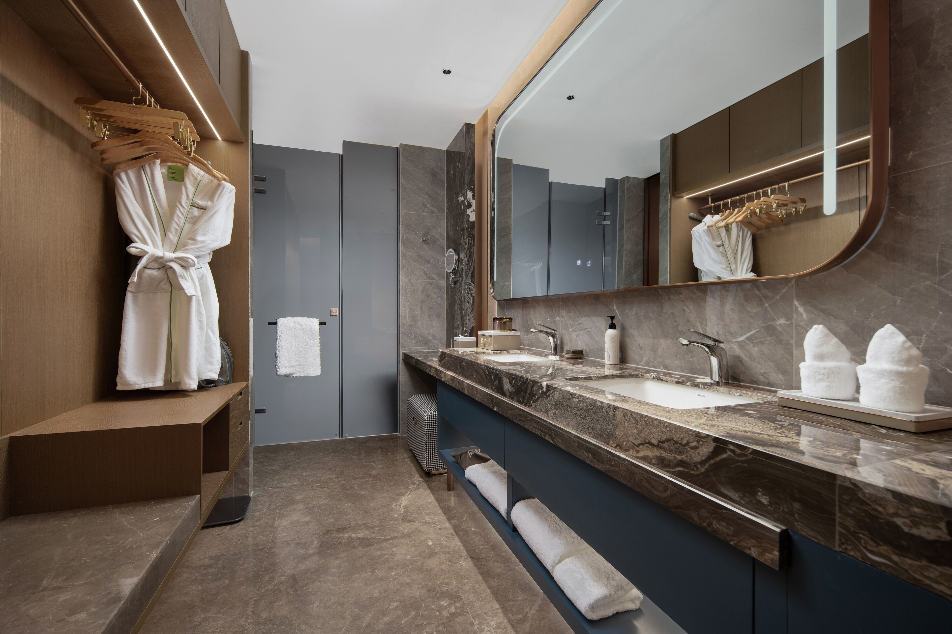 A modern bathroom with a marble countertop, dual sinks, a large mirror, and a robe rack.