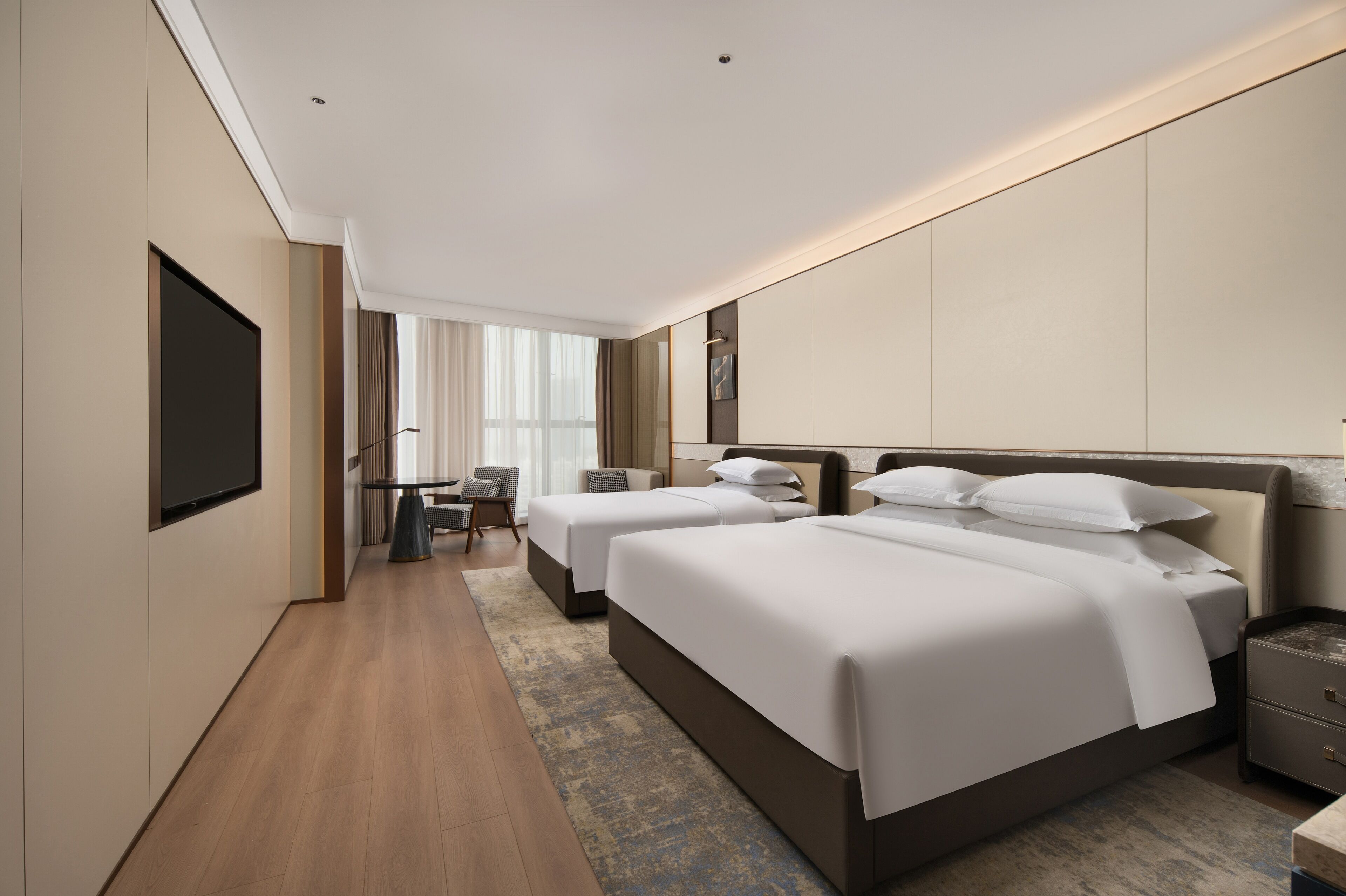 A hotel room with two beds, a desk, and a TV.
