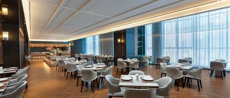 Un restaurant spacieux avec de hauts plafonds, un éclairage moderne et de grandes fenêtres.