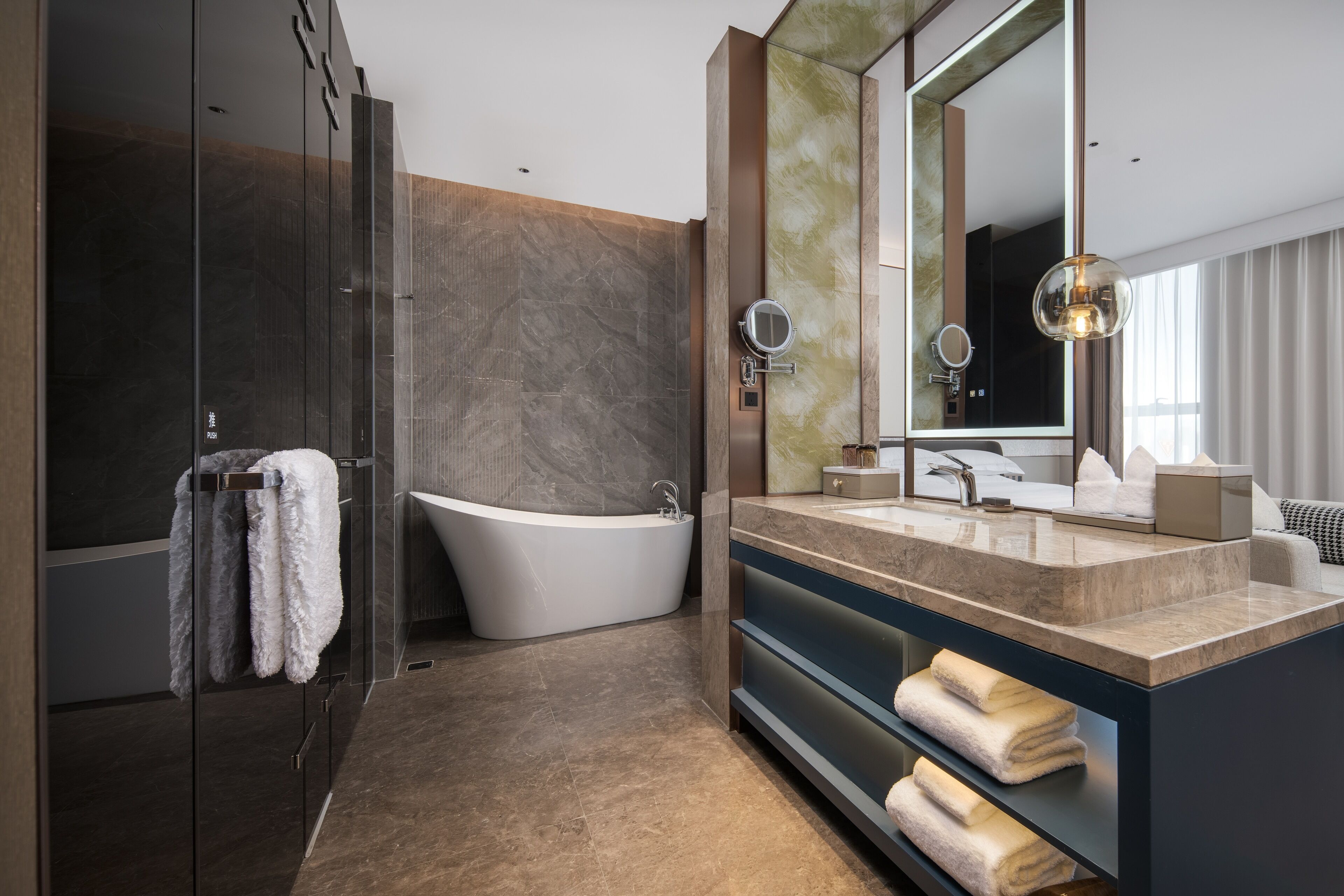 A modern bathroom with a freestanding bathtub, a large mirror, and built-in shelves for towels.