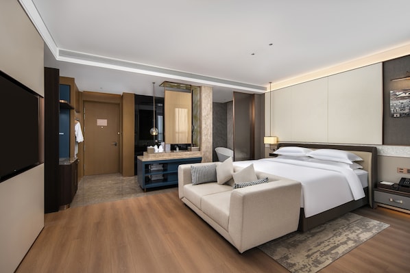 Una habitación de hotel con cama, sofá, escritorio, espejo y armario.