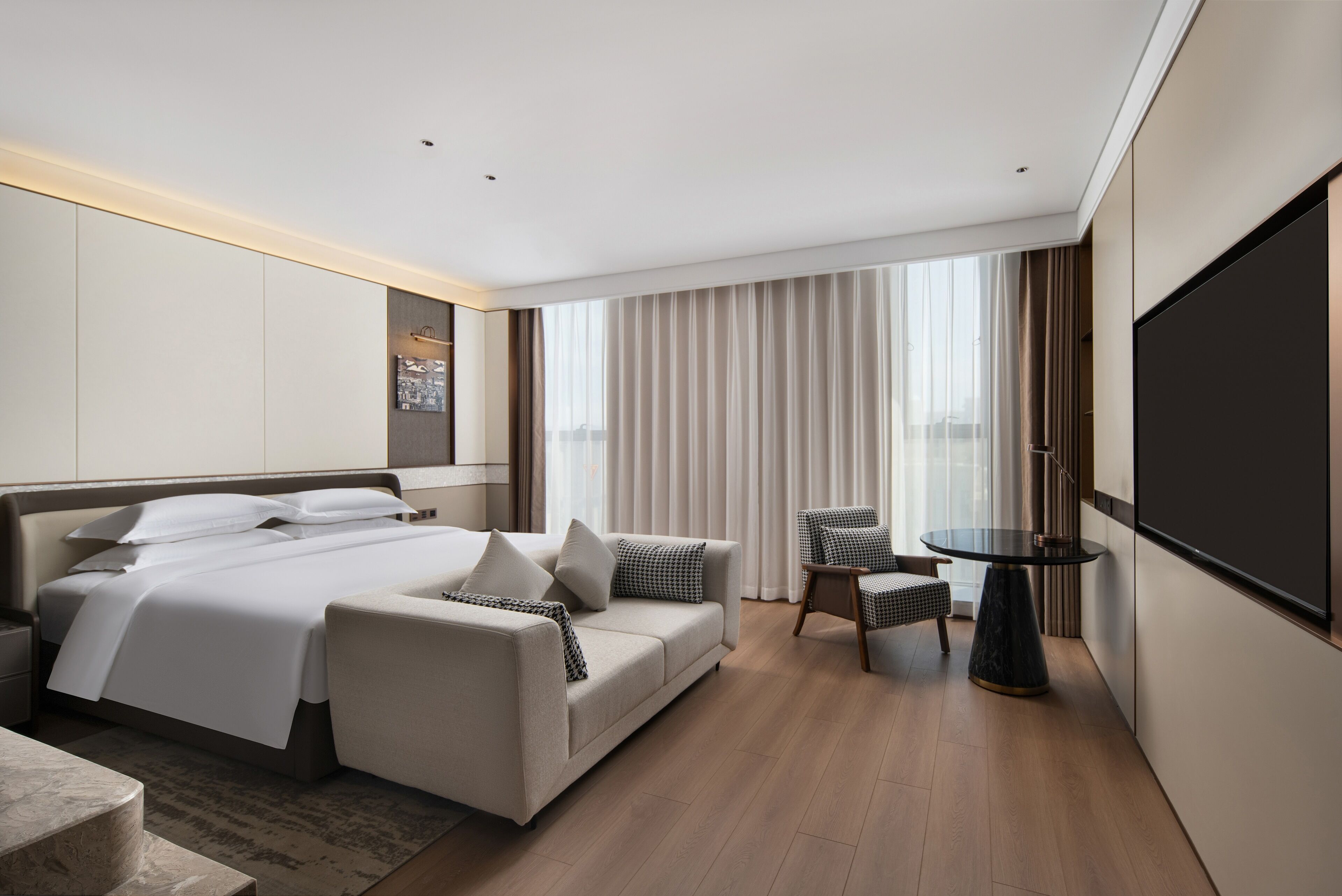 Una habitación de hotel moderna con una cama grande, un sofá, una mesita y un televisor.