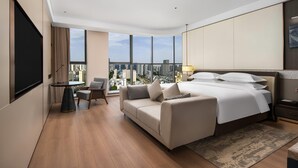 Ein modernes Hotelzimmer mit einem großen Bett, einer Couch, einem Esstisch und Blick auf die Stadt.