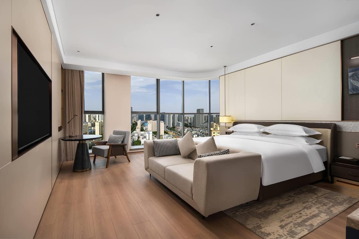 Une chambre d’hôtel moderne dotée d’un grand lit, d’un canapé, d’une table à manger et offrant une vue sur la ville.