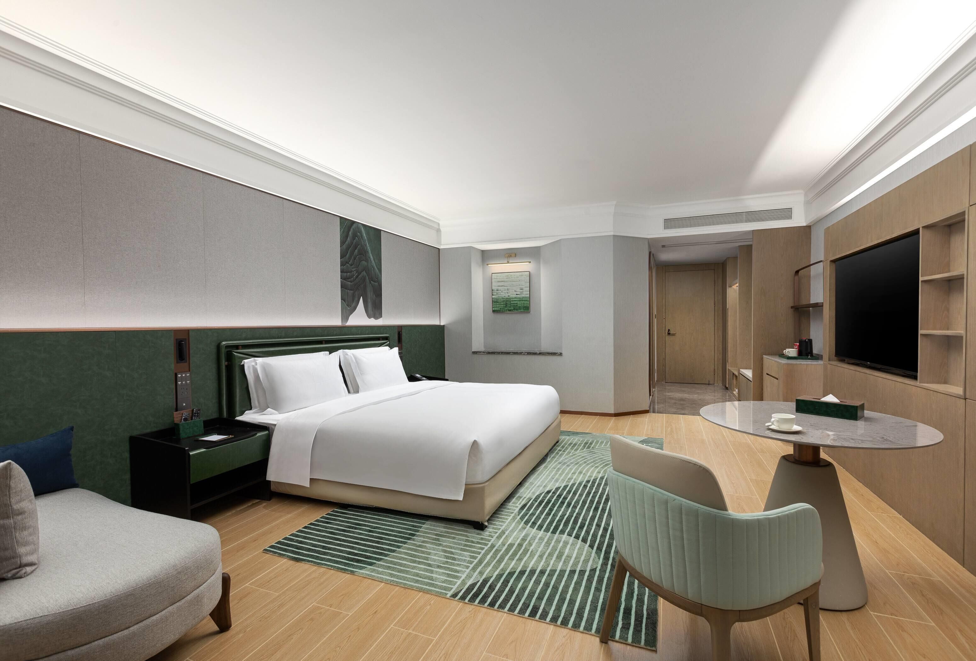 A modern hotel room with a large bed, a desk with a chair, a TV, and a small table.