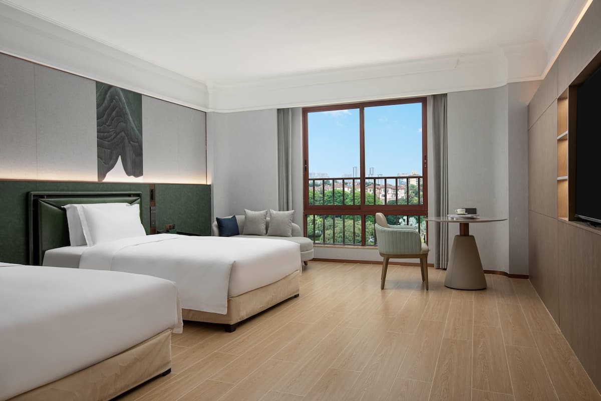 A hotel room with two beds, a balcony with a view, a small table, and a TV.