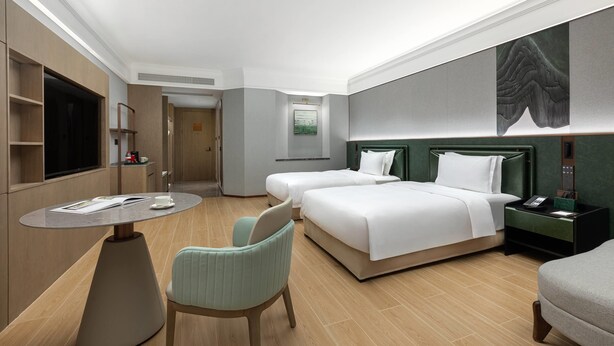 A hotel room with a bed, two bedside tables, a chair, a small table, a TV, and a painting on the wall. - Wyndham Garden Guangzhou Panyu (Guangzhou)