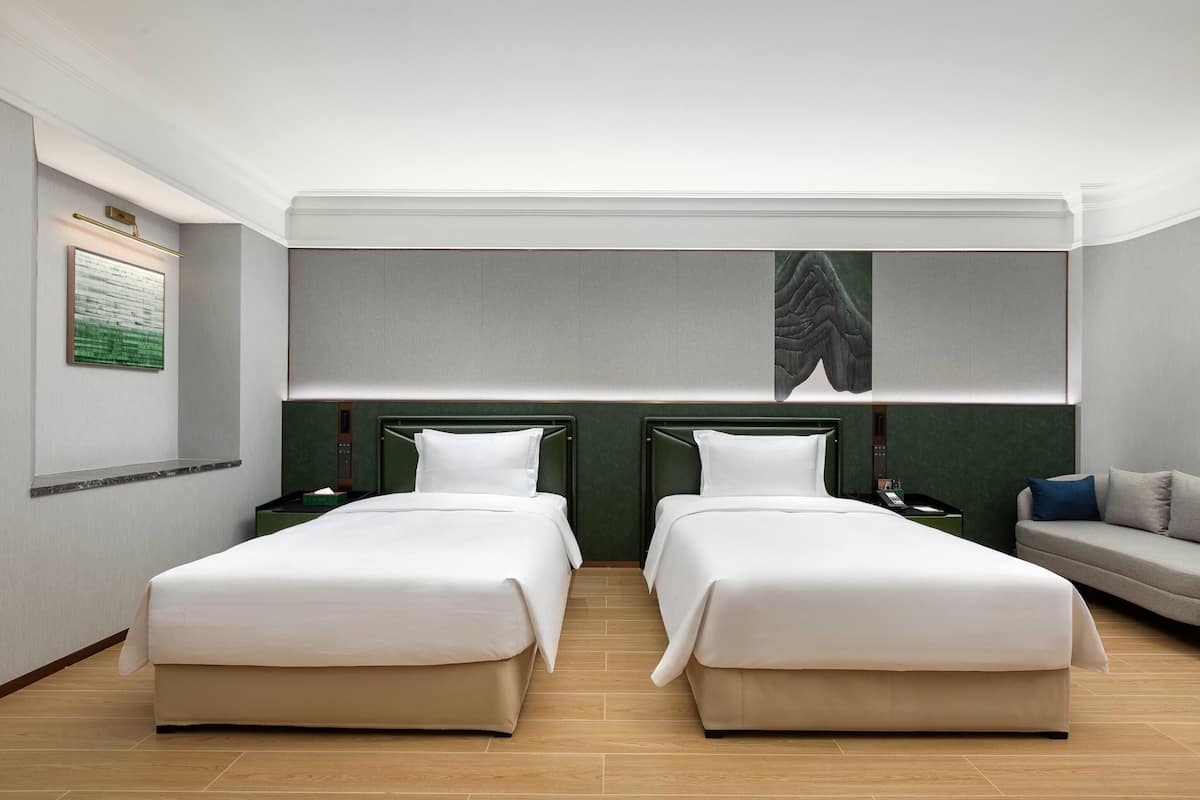 A hotel room with two beds, a sofa, and a large mirror.