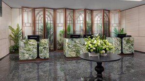 Un espace d’accueil doté d’un comptoir de réception en marbre, d’une cloison décorative et d’une table ronde agrémentée d’un arrangement floral.