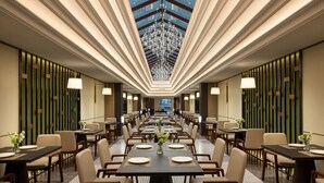 Une vaste salle à manger d’hôtel, dotée de longues tables, de chaises et d’un lustre central.