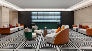 A modern lobby with a geometric patterned floor, a central seating area with orange and white sofas, and a bar area with illuminated shelves. - Wyndham Garden Guangzhou Panyu (Guangzhou)