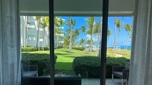 A room with a large sliding glass door leading to a balcony with a view of a golf course, palm trees, and a building with a pool. - beach paradise ground floor Cabarete (Cabarete)
