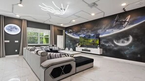 A modern living room with a sectional sofa, a flat-screen TV, and a wall mural depicting space.