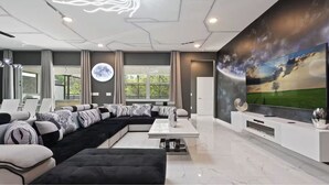 A modern living room with a sectional sofa, a flat-screen TV, and a large window with a view of greenery.