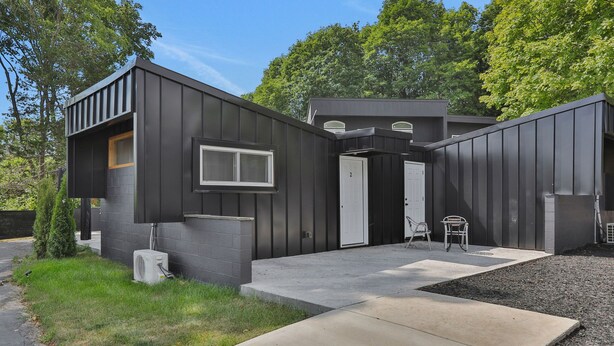 A modern two-story house with a dark exterior, a front porch, and a small outdoor seating area. - Overlook Hotel (Saugerties)
