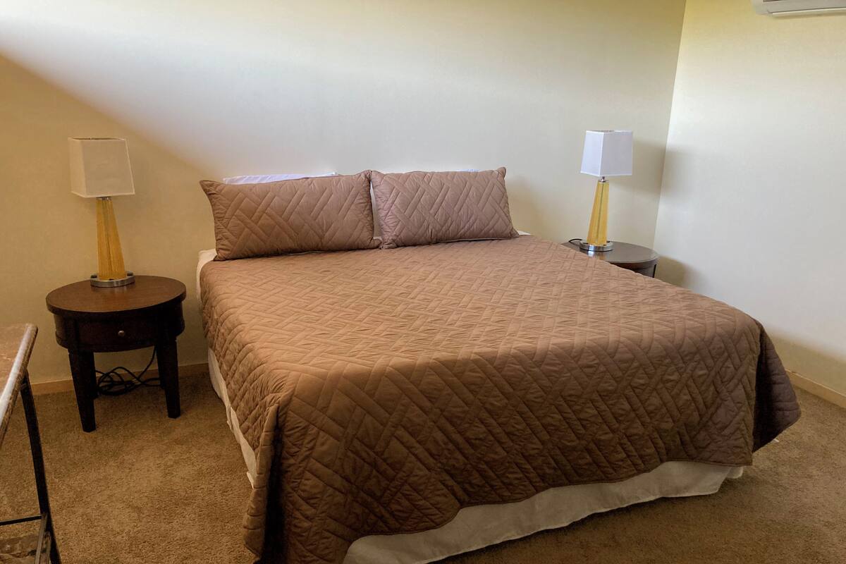 A neatly made bed with a brown quilted bedspread and two pillows, flanked by two bedside tables with lamps.