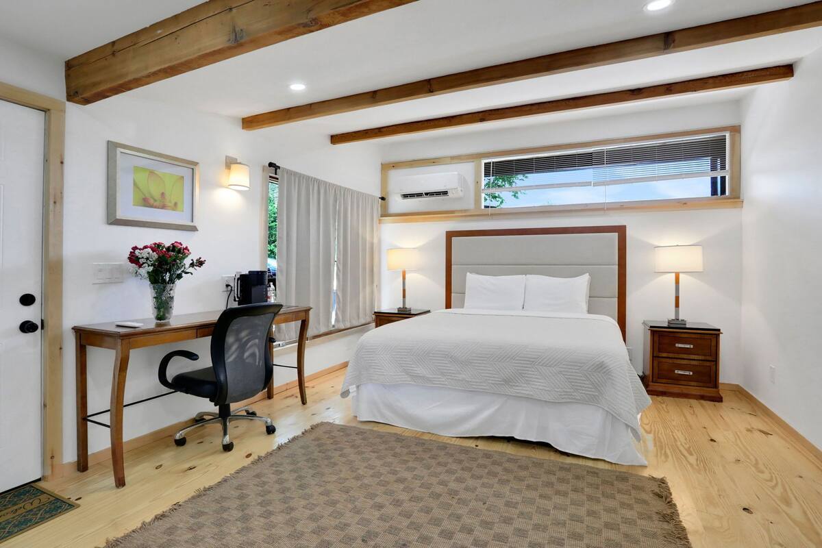 A bedroom with a bed, desk, chair, and bedside tables.