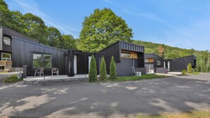 A modern building with a large driveway, a covered outdoor seating area, and a large tree in the background. - Overlook Hotel (Saugerties)