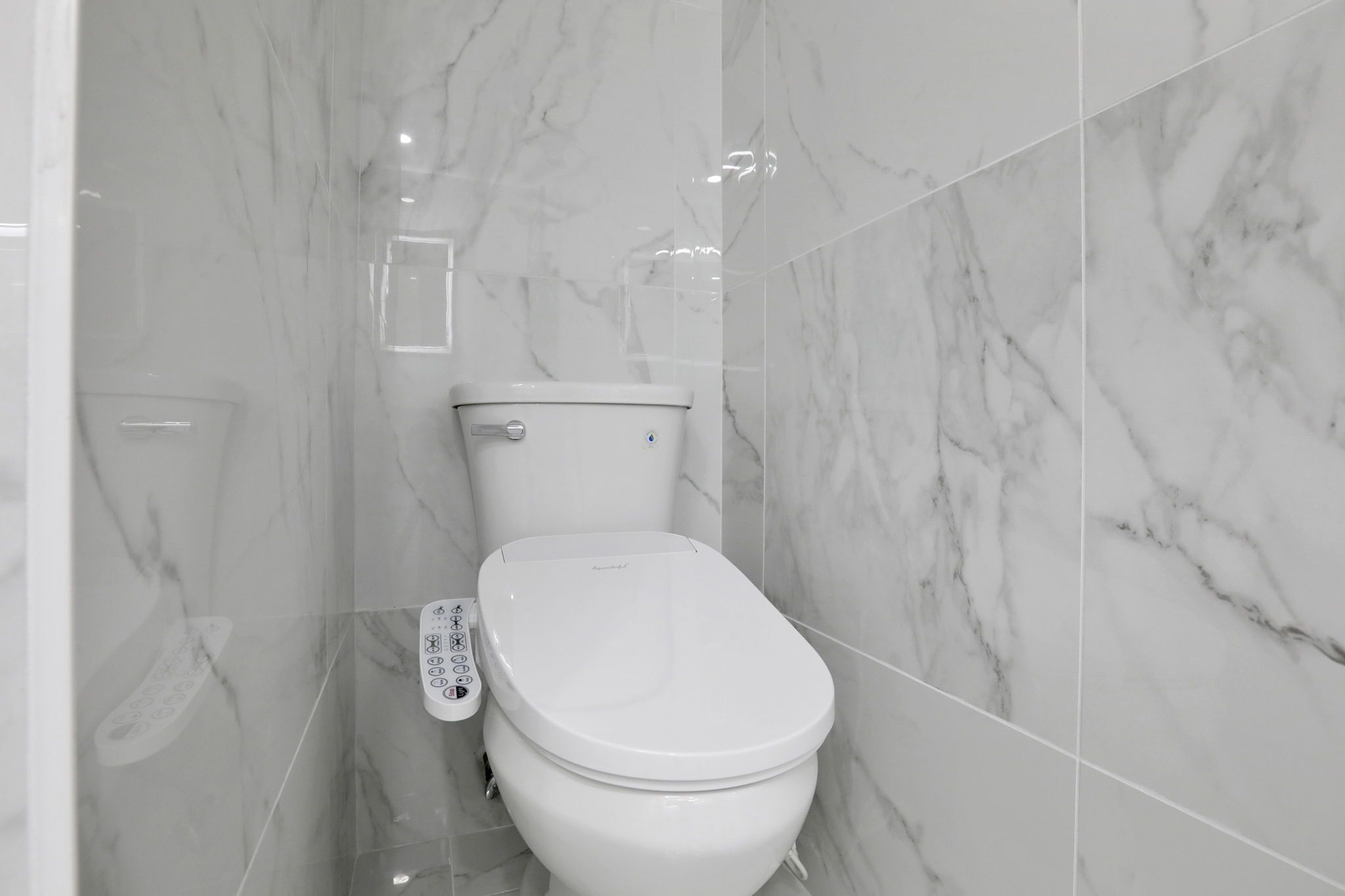 A modern bathroom with a white toilet, marble walls, and a control panel.