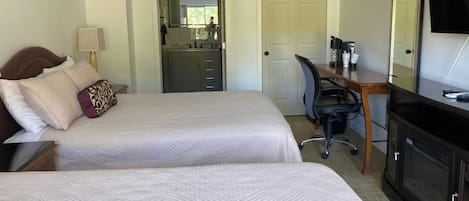 Habitación de hotel con dos camas, un escritorio, una silla, un televisor y un baño visible a través de una puerta abierta.