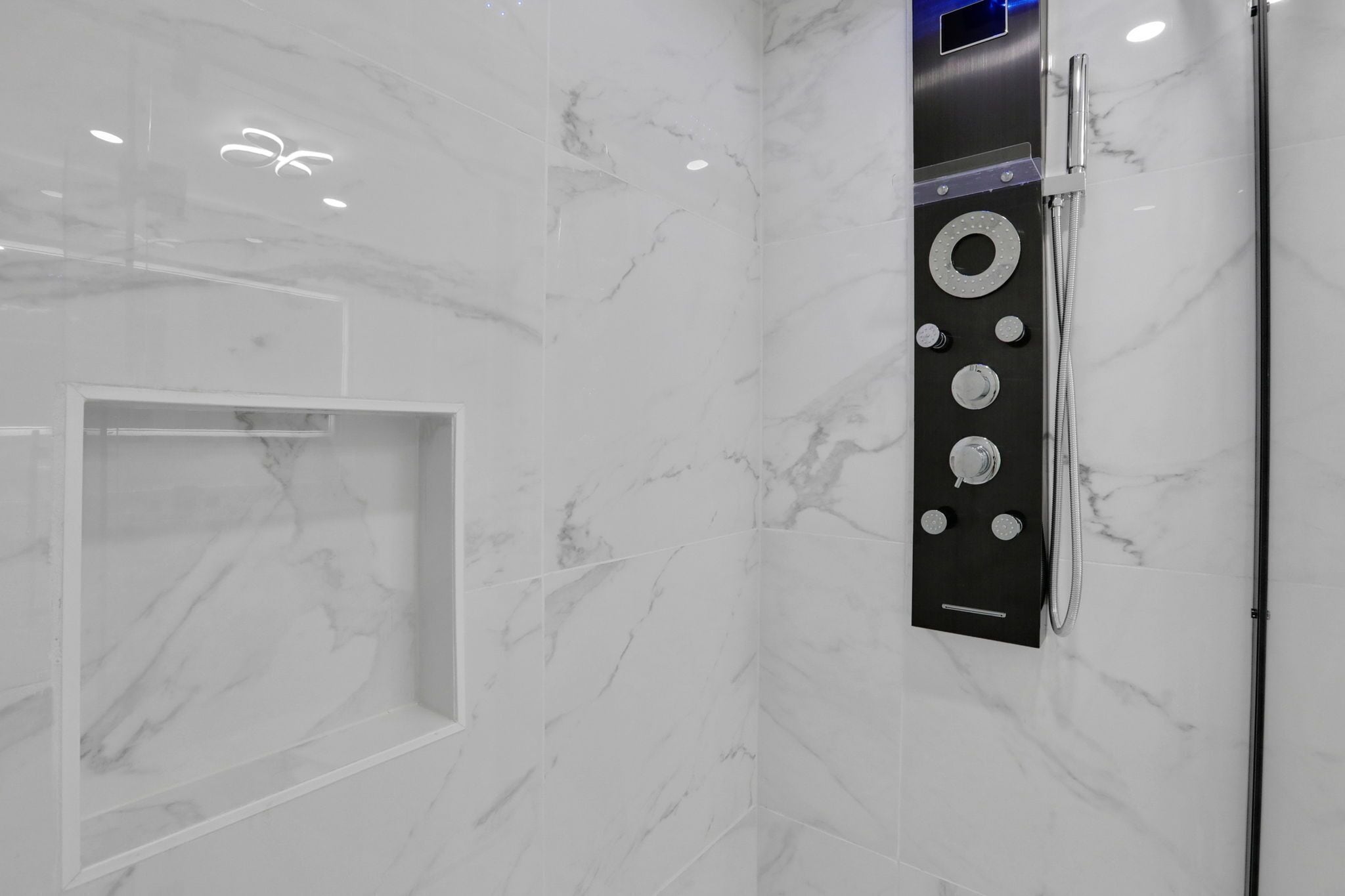 Un baño moderno con paredes de mármol, ducha empotrada con varios controles y cabina de ducha con mampara de vidrio.
