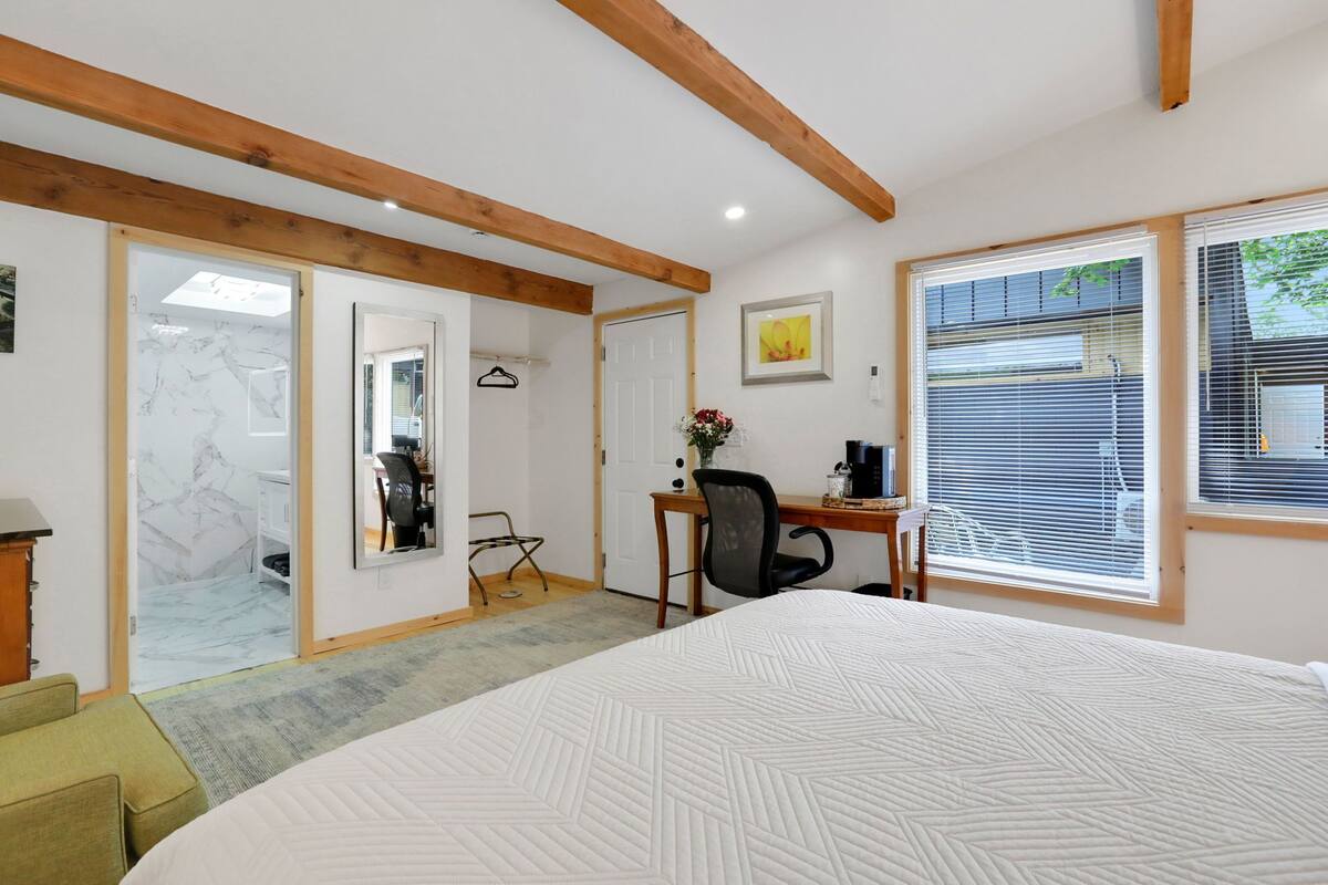 A bedroom with a large bed, a desk with a chair, a wardrobe, and a door leading to a bathroom.