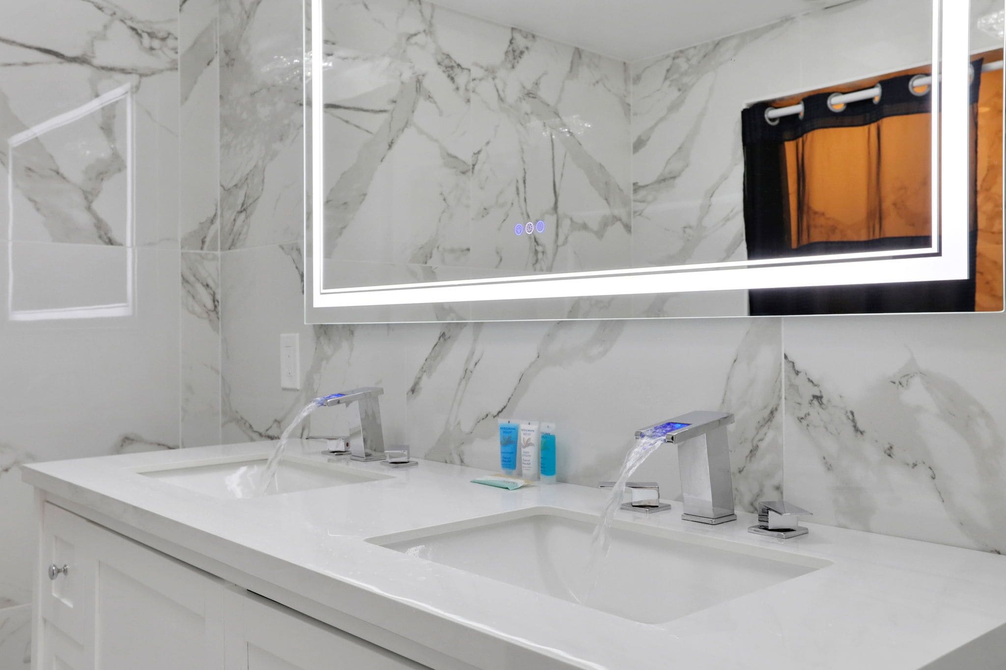 A modern bathroom with two sinks, a large mirror, and marble walls.