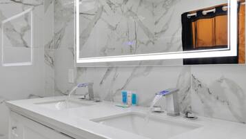 A modern bathroom with two sinks, a large mirror, and marble walls.