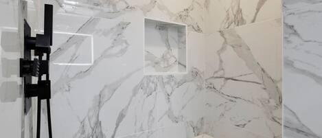Une salle de bain aux murs recouverts de marbre, dotée d’une douche en verre et d’un meuble-lavabo blanc.